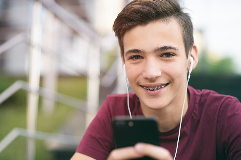 Close Up Portrait Of A Smiling Young Man With A Smartphone, In T